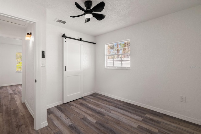 unfurnished bedroom featuring a barn door, baseboards, visible vents, dark wood-type flooring, and a textured ceiling