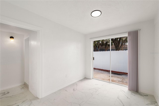 empty room featuring a textured ceiling, marble finish floor, and baseboards