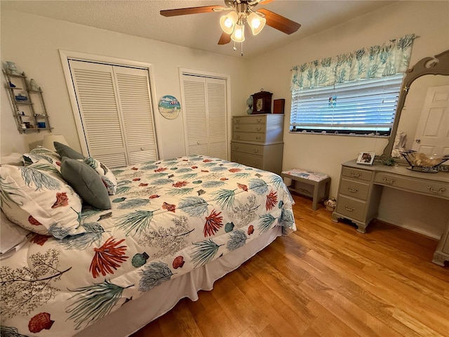 bedroom featuring light wood-type flooring, ceiling fan, a textured ceiling, and two closets