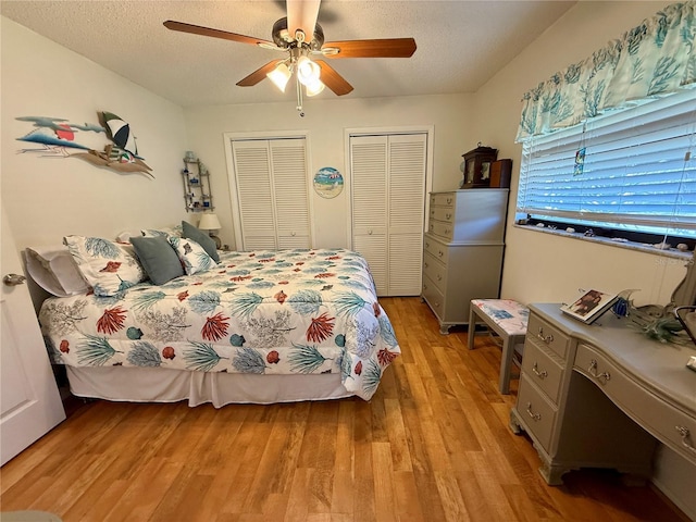 bedroom with a textured ceiling, ceiling fan, light wood-style floors, and multiple closets