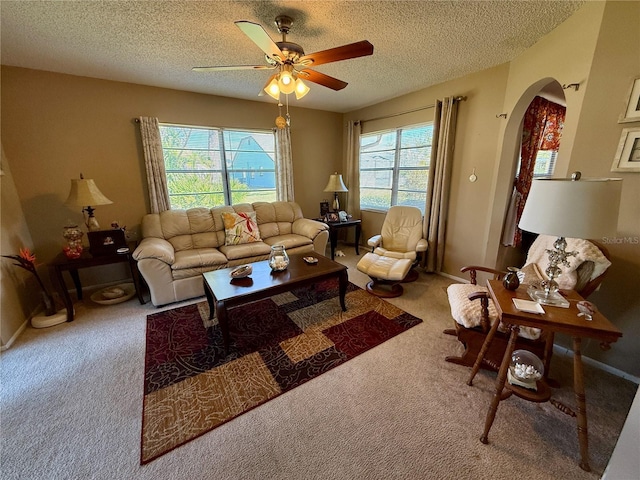 living room with arched walkways, a textured ceiling, carpet floors, a ceiling fan, and baseboards