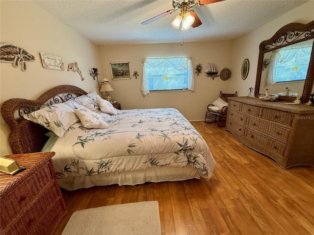 bedroom featuring a textured ceiling, ceiling fan, multiple windows, and wood finished floors