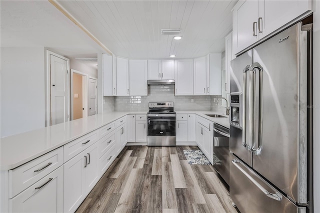 kitchen featuring decorative backsplash, appliances with stainless steel finishes, under cabinet range hood, white cabinetry, and a sink