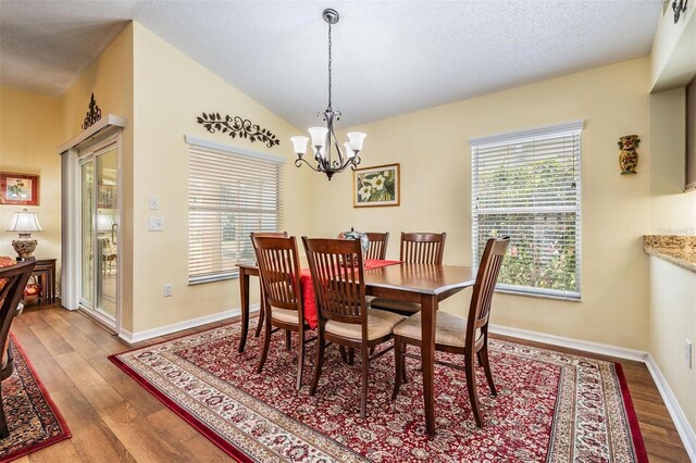 dining room with a notable chandelier, vaulted ceiling, a textured ceiling, wood finished floors, and baseboards