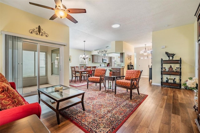 living room featuring baseboards, hardwood / wood-style floors, vaulted ceiling, a textured ceiling, and ceiling fan with notable chandelier