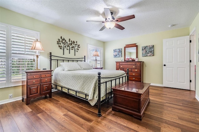 bedroom with a ceiling fan, a textured ceiling, baseboards, and dark wood-style flooring