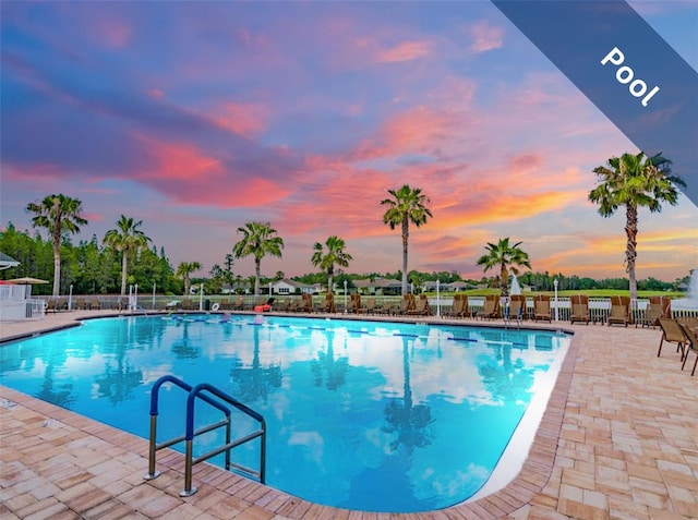 pool at dusk featuring a patio area, fence, and a community pool