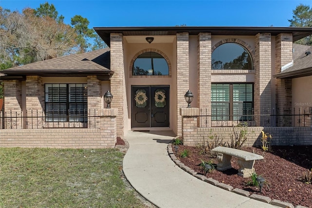 doorway to property featuring a shingled roof, french doors, and brick siding