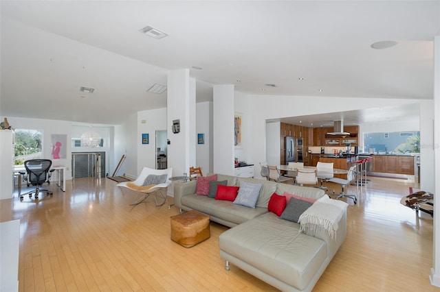 living area with light wood finished floors, visible vents, vaulted ceiling, and a notable chandelier