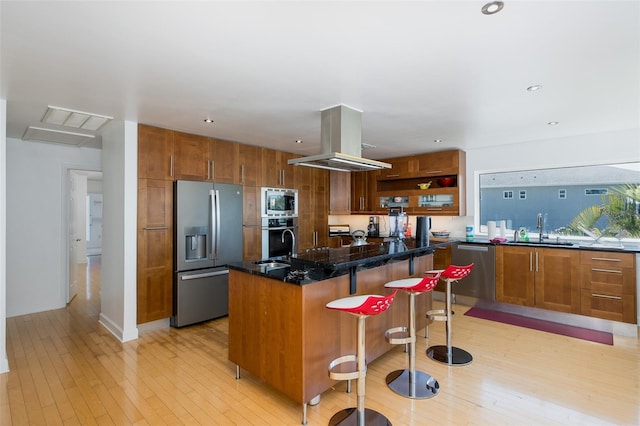 kitchen with light wood-style flooring, island range hood, a sink, appliances with stainless steel finishes, and brown cabinets