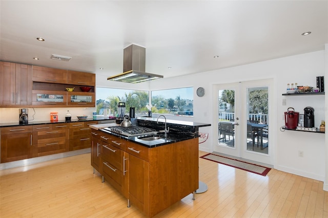 kitchen featuring island range hood, french doors, light wood-type flooring, open shelves, and an island with sink