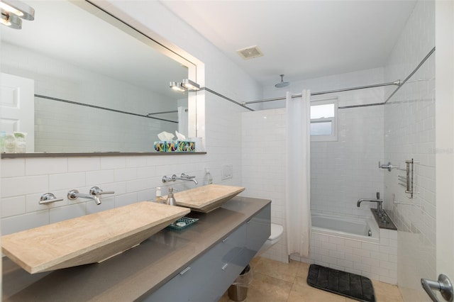 bathroom with tile patterned flooring, a combined bath / shower with rainfall shower, a sink, visible vents, and tile walls