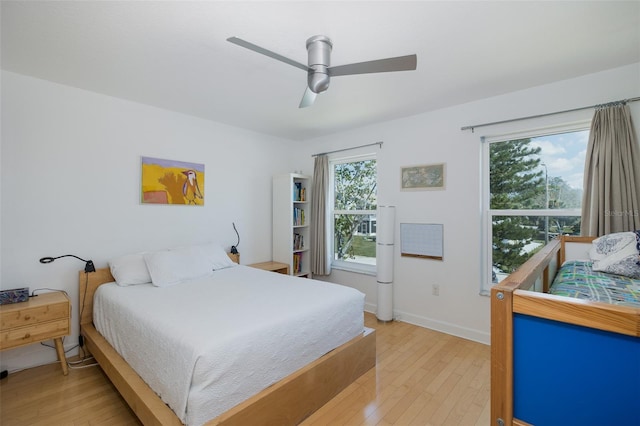 bedroom featuring light wood finished floors, multiple windows, baseboards, and a ceiling fan