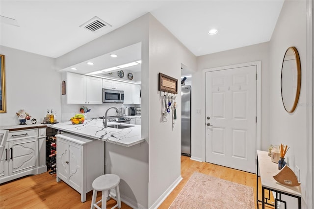 kitchen with light stone counters, visible vents, appliances with stainless steel finishes, white cabinetry, and a sink