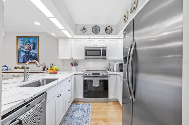 kitchen with a sink, white cabinetry, light wood-style floors, appliances with stainless steel finishes, and light stone countertops