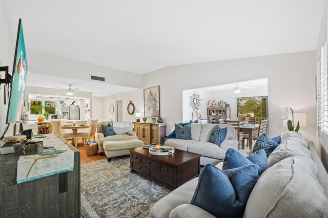 living room with a ceiling fan, visible vents, vaulted ceiling, and wood finished floors