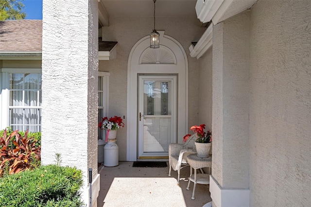 doorway to property with stucco siding and roof with shingles