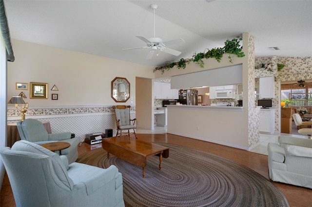 living room featuring visible vents, vaulted ceiling, wainscoting, light wood-style flooring, and a ceiling fan