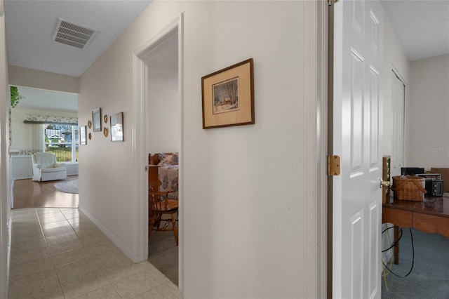 corridor featuring light tile patterned flooring, visible vents, and baseboards