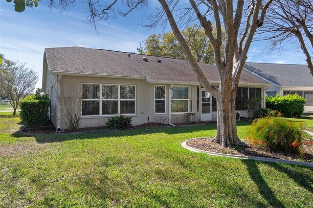 rear view of property with stucco siding, a sunroom, a yard, and roof with shingles