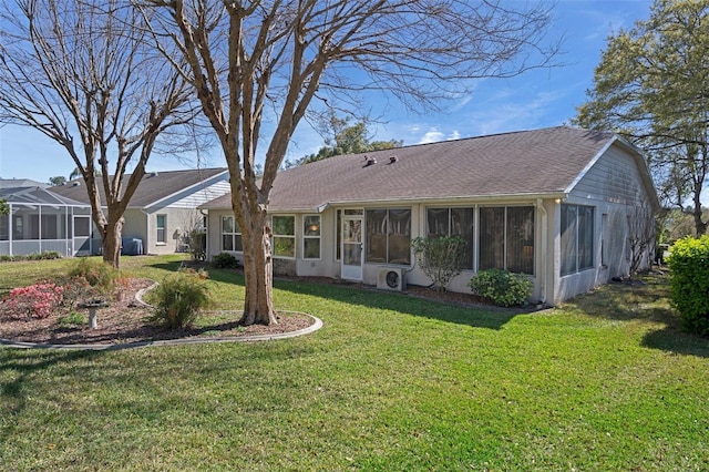 rear view of house featuring a lawn, roof with shingles, and a sunroom