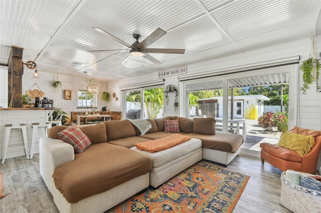 living area featuring ceiling fan, brick wall, and wood finished floors