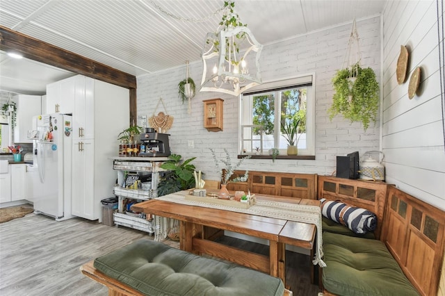 interior space featuring a notable chandelier, brick wall, beam ceiling, light wood finished floors, and breakfast area