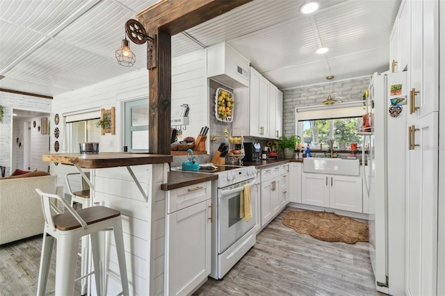 kitchen featuring white appliances, light wood finished floors, dark countertops, brick wall, and a sink