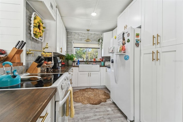 kitchen with white appliances, white cabinets, a sink, light wood-style floors, and backsplash