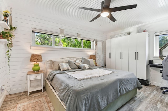 bedroom featuring wooden walls, a closet, a ceiling fan, and light wood-style floors