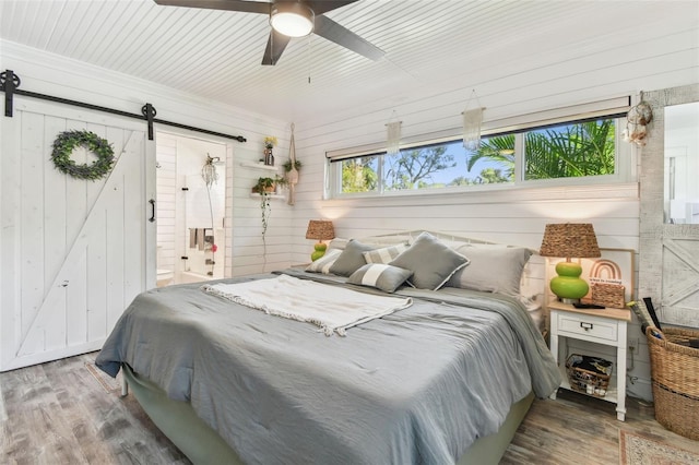 bedroom featuring ensuite bath, a barn door, a ceiling fan, and wood finished floors