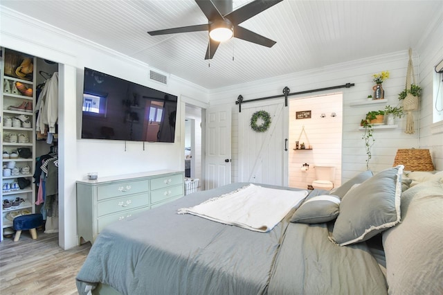 bedroom with visible vents, crown molding, light wood-style flooring, and a barn door