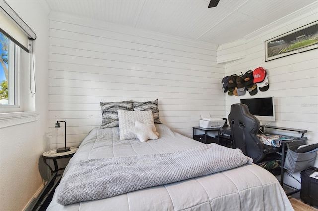 bedroom featuring wooden walls, ornamental molding, and a ceiling fan