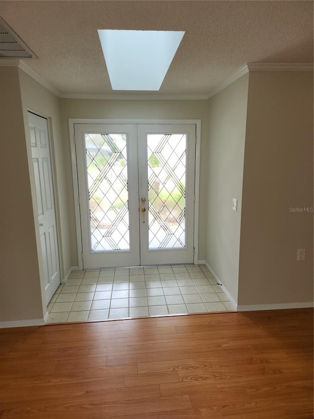 entryway with a textured ceiling, french doors, ornamental molding, and light wood-type flooring