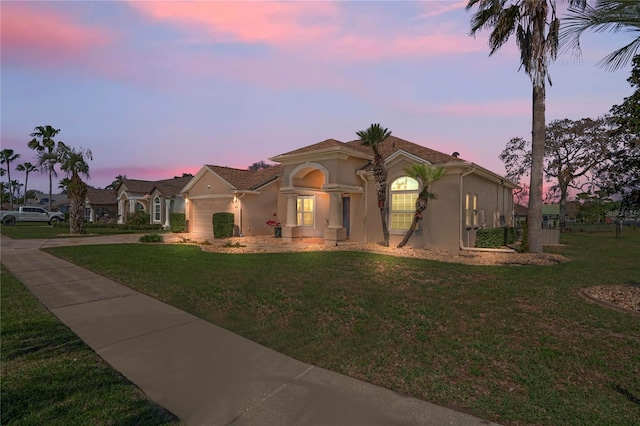 mediterranean / spanish house with a garage, a front yard, driveway, and stucco siding