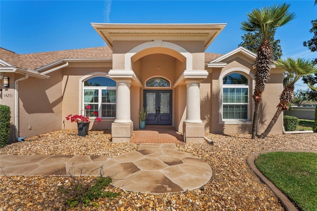 entrance to property with stucco siding, roof with shingles, and french doors