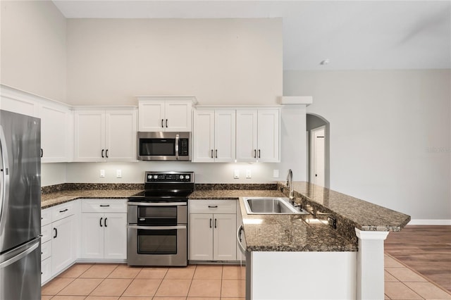 kitchen with white cabinets, appliances with stainless steel finishes, a peninsula, a sink, and light tile patterned flooring