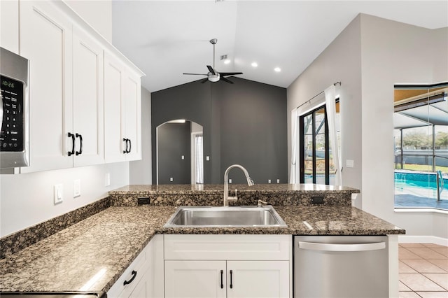 kitchen with a sink, a ceiling fan, white cabinetry, appliances with stainless steel finishes, and dark stone counters