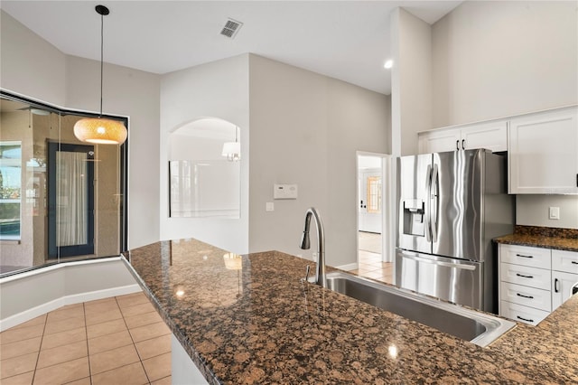 kitchen featuring arched walkways, stainless steel fridge, visible vents, and white cabinetry