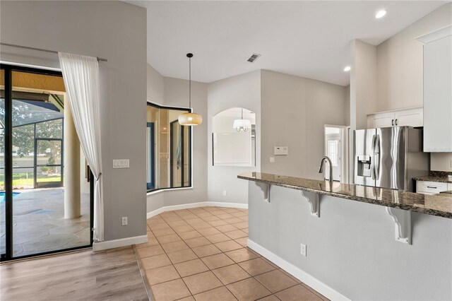 kitchen with visible vents, white cabinets, baseboards, a kitchen breakfast bar, and stainless steel fridge