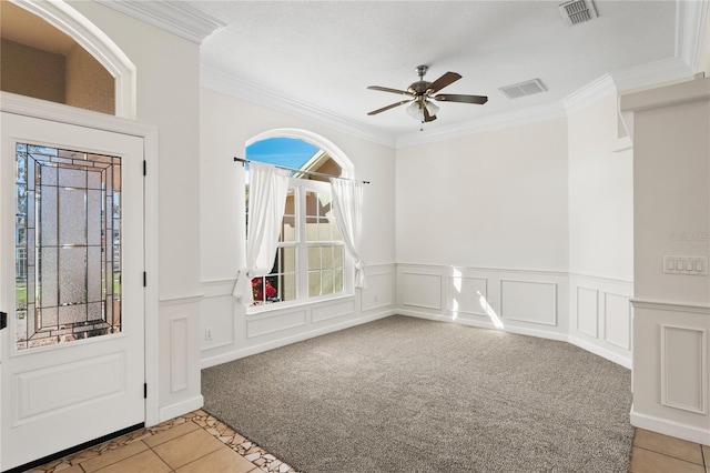 foyer entrance with light carpet, ceiling fan, visible vents, and crown molding