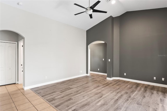 empty room with arched walkways, a ceiling fan, light wood-style floors, high vaulted ceiling, and baseboards