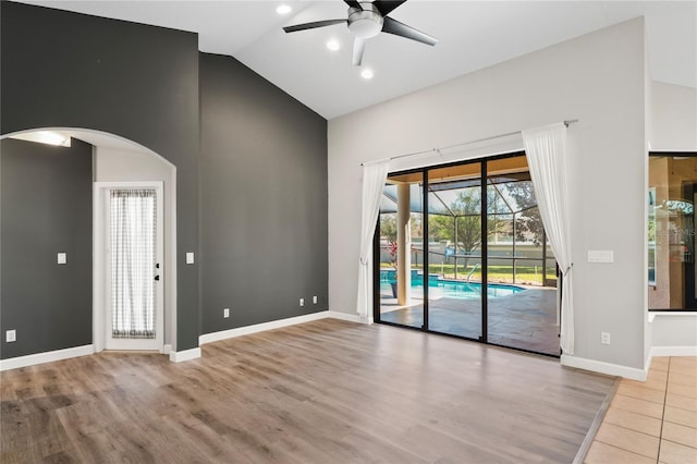 spare room with baseboards, arched walkways, lofted ceiling, ceiling fan, and wood finished floors