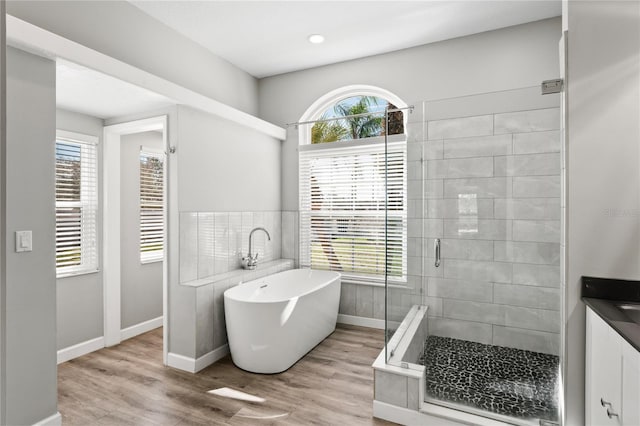 bathroom featuring a stall shower, baseboards, a freestanding bath, and wood finished floors