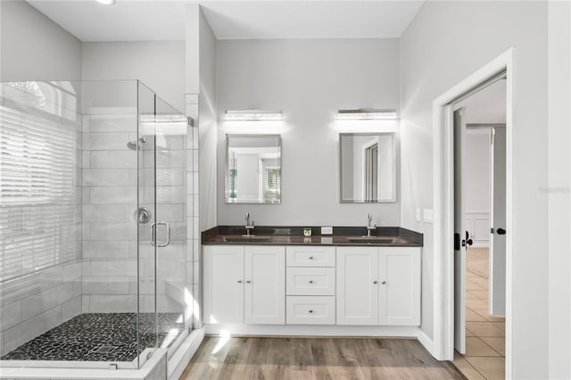 bathroom with a stall shower, wood finished floors, a sink, and double vanity