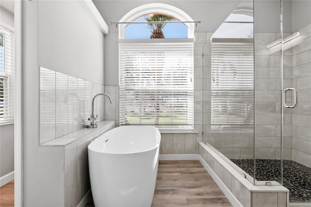 bathroom with a healthy amount of sunlight, a freestanding bath, a shower stall, and wood finished floors