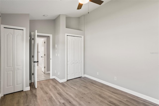 unfurnished bedroom featuring lofted ceiling, baseboards, two closets, and wood finished floors