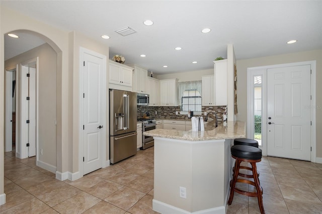 kitchen featuring visible vents, arched walkways, appliances with stainless steel finishes, a peninsula, and a kitchen bar