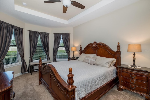 bedroom featuring a raised ceiling, light colored carpet, ceiling fan, and baseboards