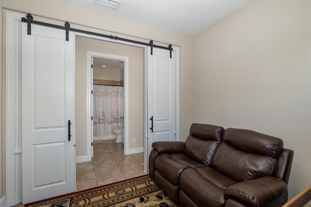 living area with light tile patterned floors, visible vents, baseboards, and a barn door